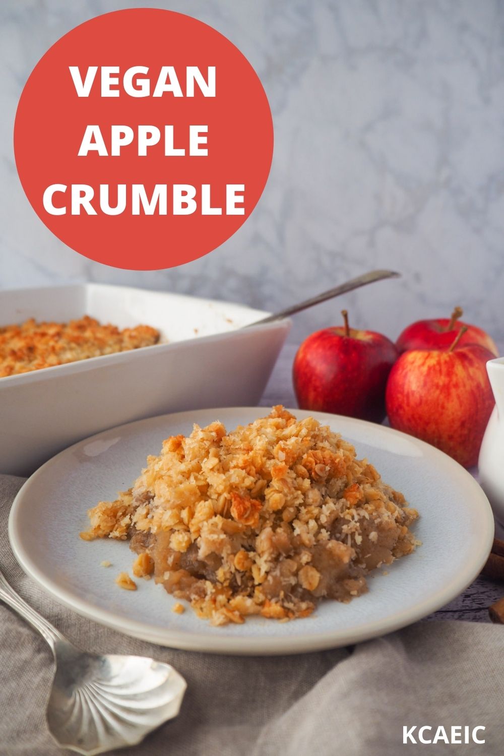 Vegan apple crumble on a plate with crumble and fresh apples in the background, and text overlay, vegan apple crumble and KCAEIC.