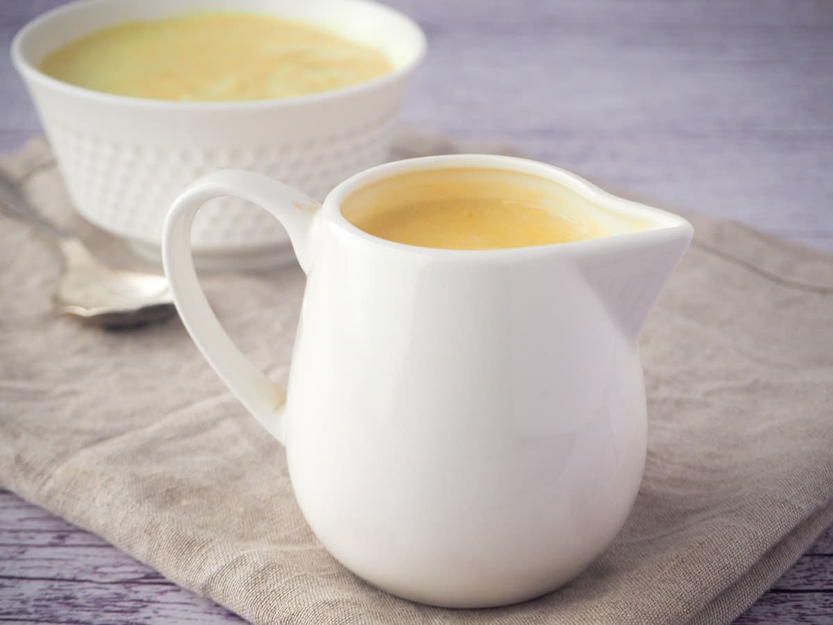 Jug of vegan custard with a bowl of custard in the background.