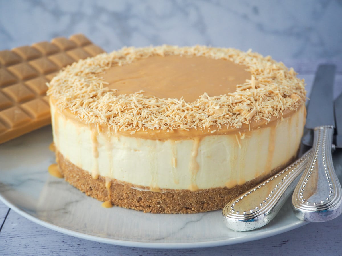 Whole caramilk cheesecake on a plate with serving silverware.