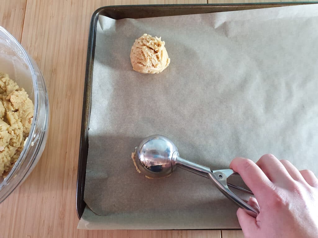 Scooping chilled cookie dough onto lined baking trays with an ice cream scoop.