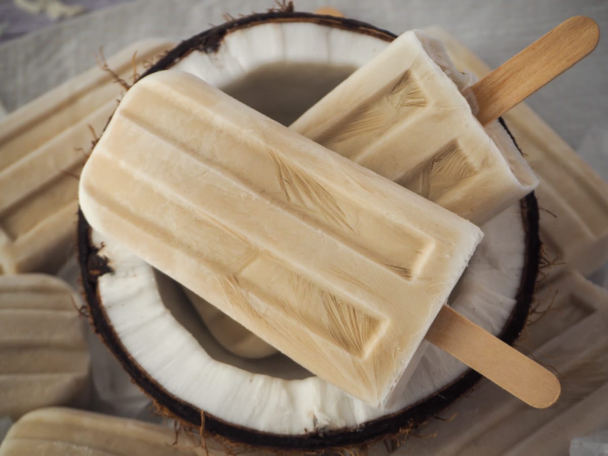 Two coconut popsicles in half a fresh coconut, with more popsicles around the edges.