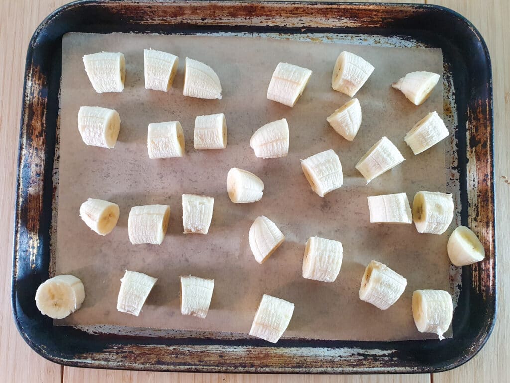 Laying out sliced bananas on a baking tray lined with baking paper, with pieces not touching each other.