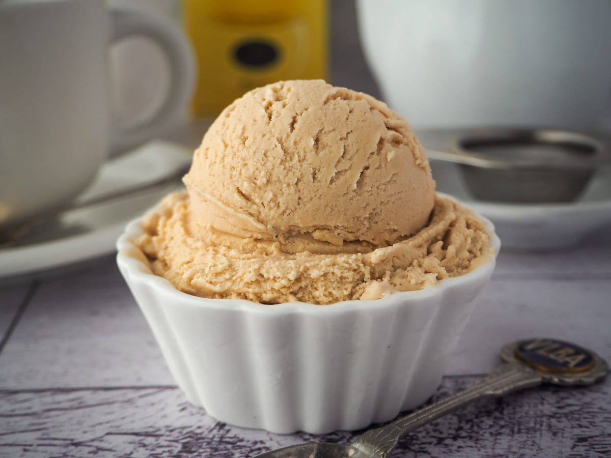 Earl grey ice cream with spoon, tea strainer and cup of tea in the background.