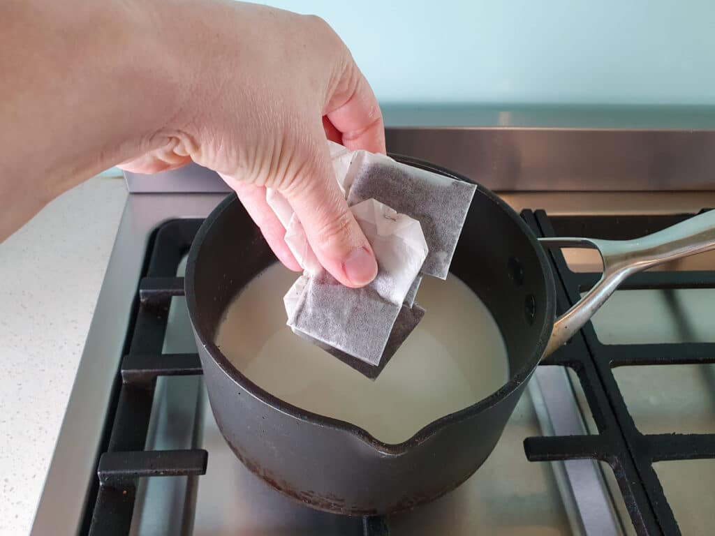 Adding tea bags to simmering milk.