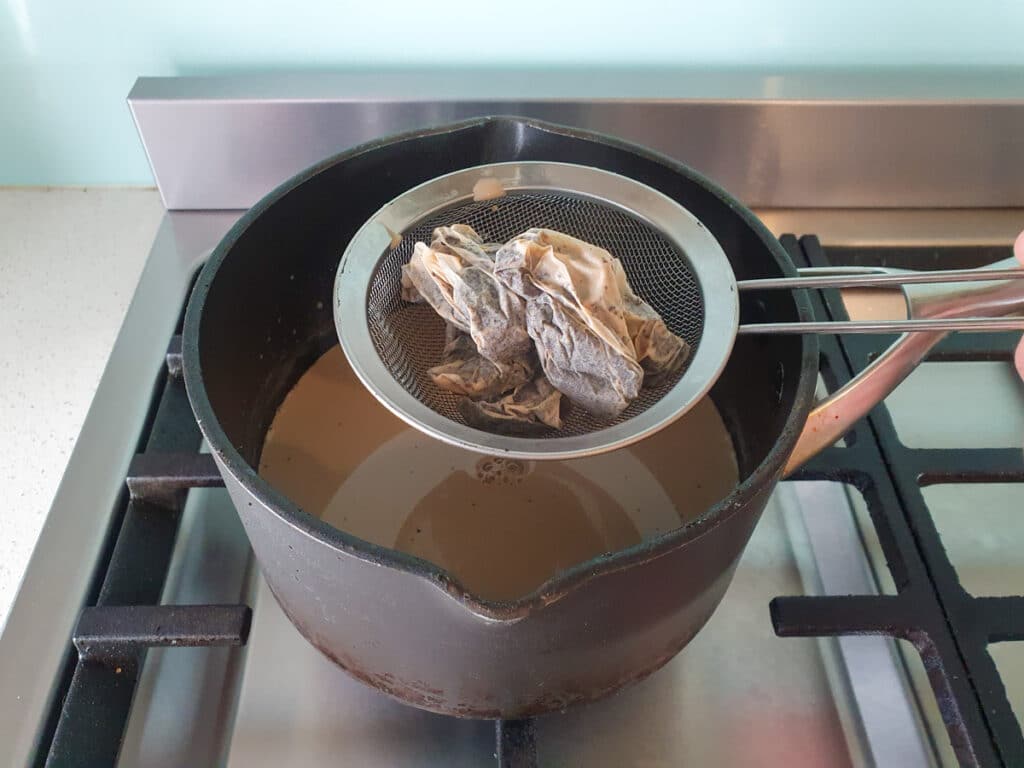 Straining tea bags over pot.