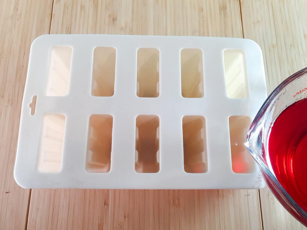 Pouring jello mix into popsicle molds.