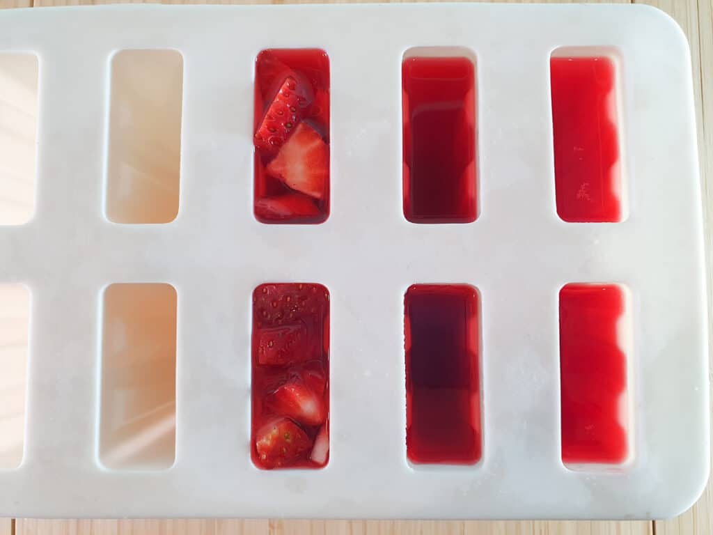 Adding strawberry pieces to popsicles.