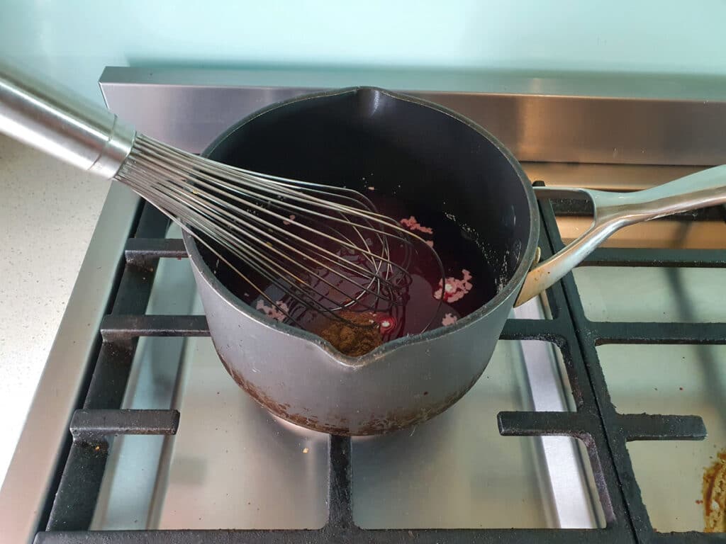 Whisking cinnamon, corn flour, lemon juice and sugar into draining cherry juice in pot on stove.