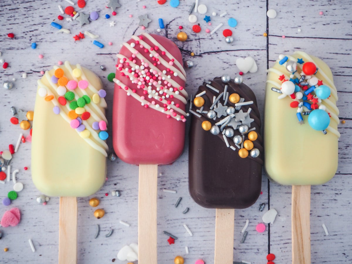 Row of three cake pops with different decorations, funfetti, valentines, silver and gold and red, white and blue.