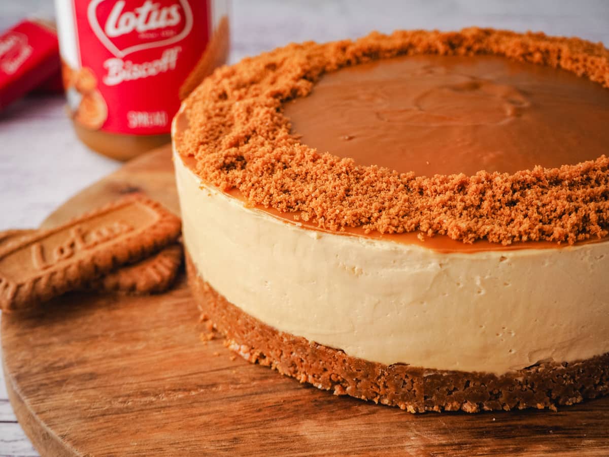 Cheesecake on a serving board with jar of Biscoff and Biscoff cookies in background.