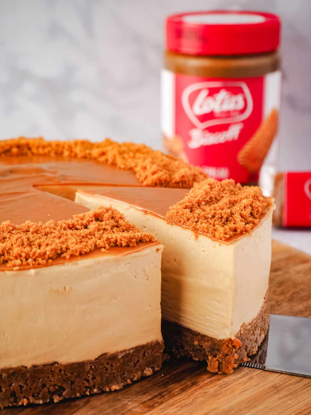Slice being taken out of cheesecake, with jar of Biscoff in the background.