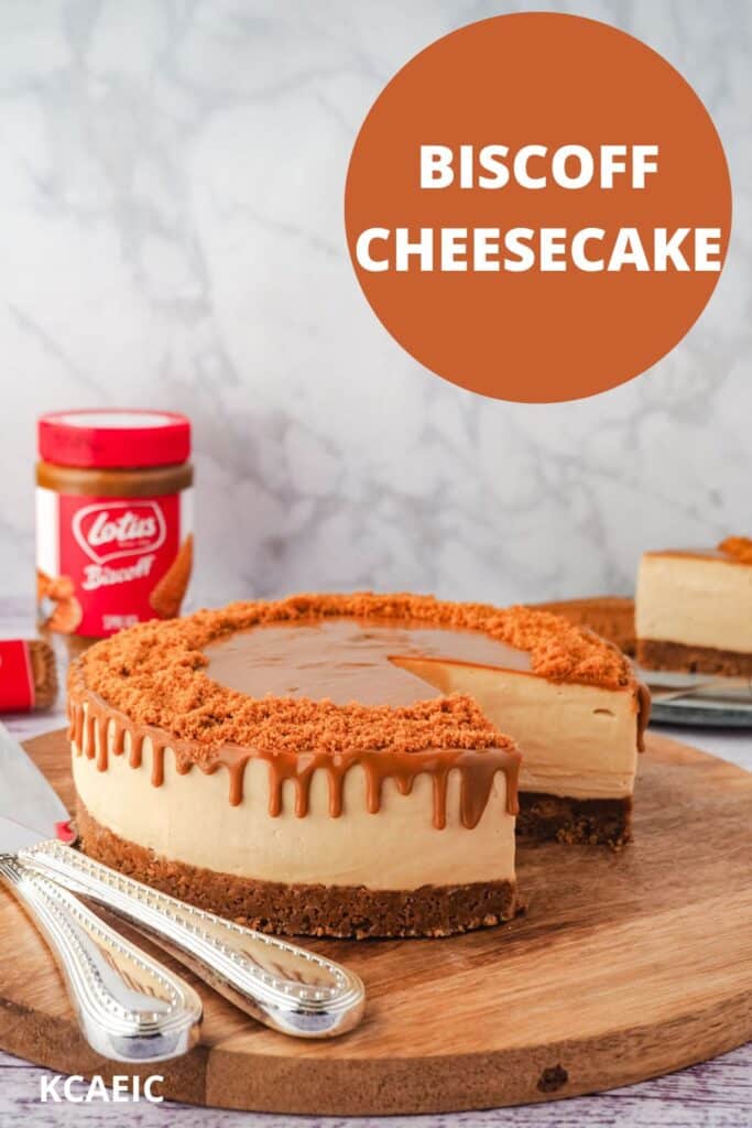 Cheesecake on a serving board with serving wear, jar of Biscoff and Biscoff cookies and slice of cake in background, with text overlay, Biscoff Cheesecake and KCAEIC.