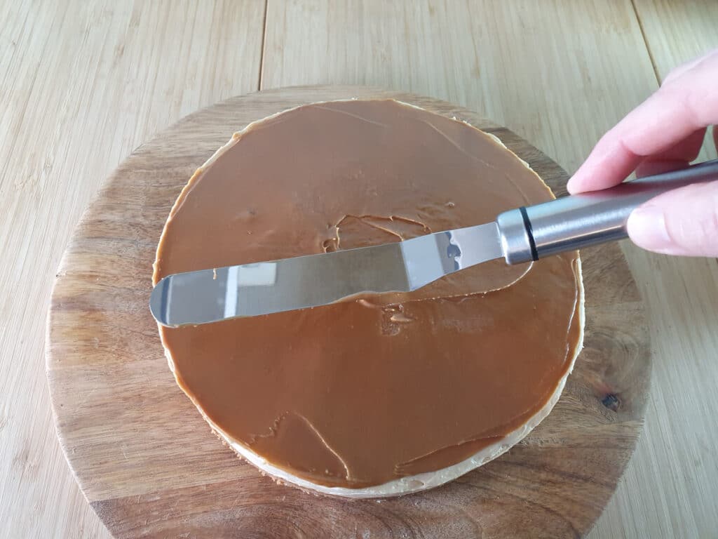 Smoothing melted biscoff onto the top of the cheesecake with an offset spatula.