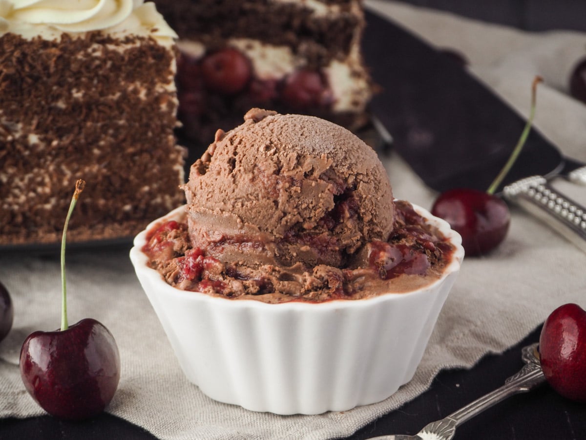 Ice cream with black forest cake in back ground and fresh cherries.