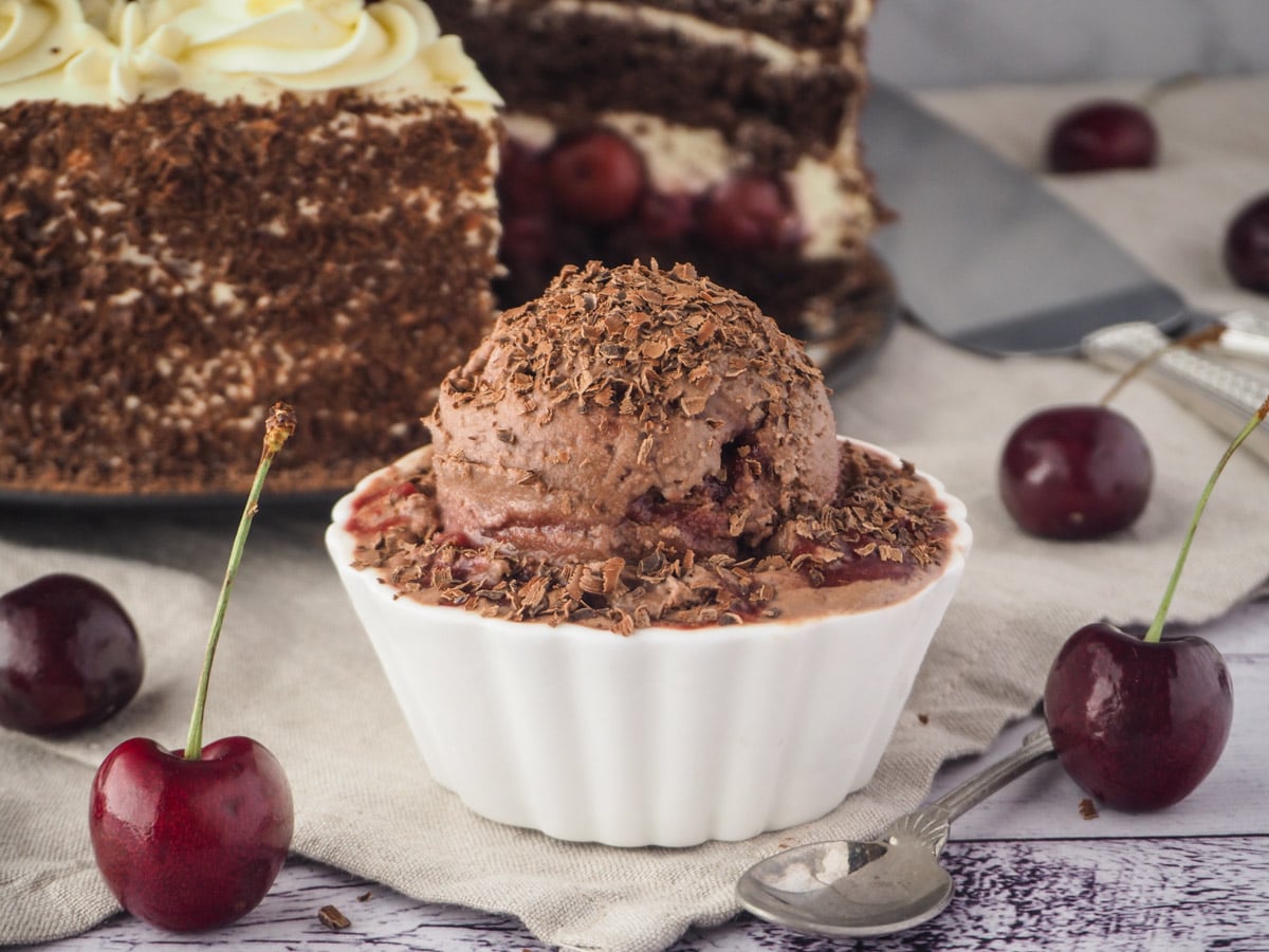 Ice cream with black forest cake in back ground and fresh cherries.