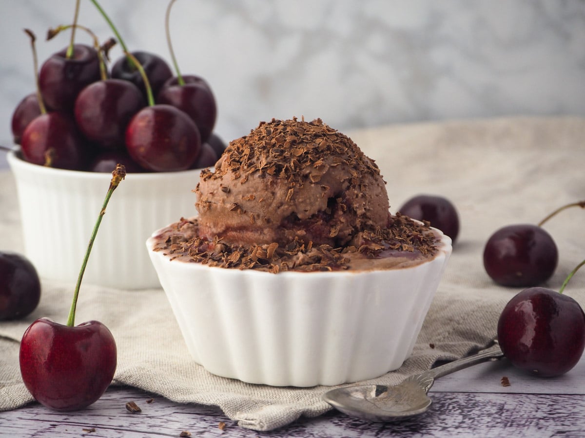 Ice cream with a spoon and fresh cherries in the background.