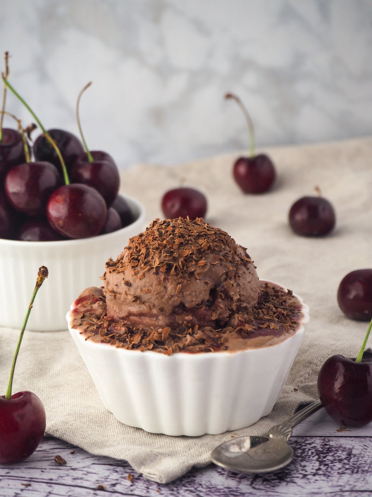 Ice cream with a spoon and fresh cherries in the background.