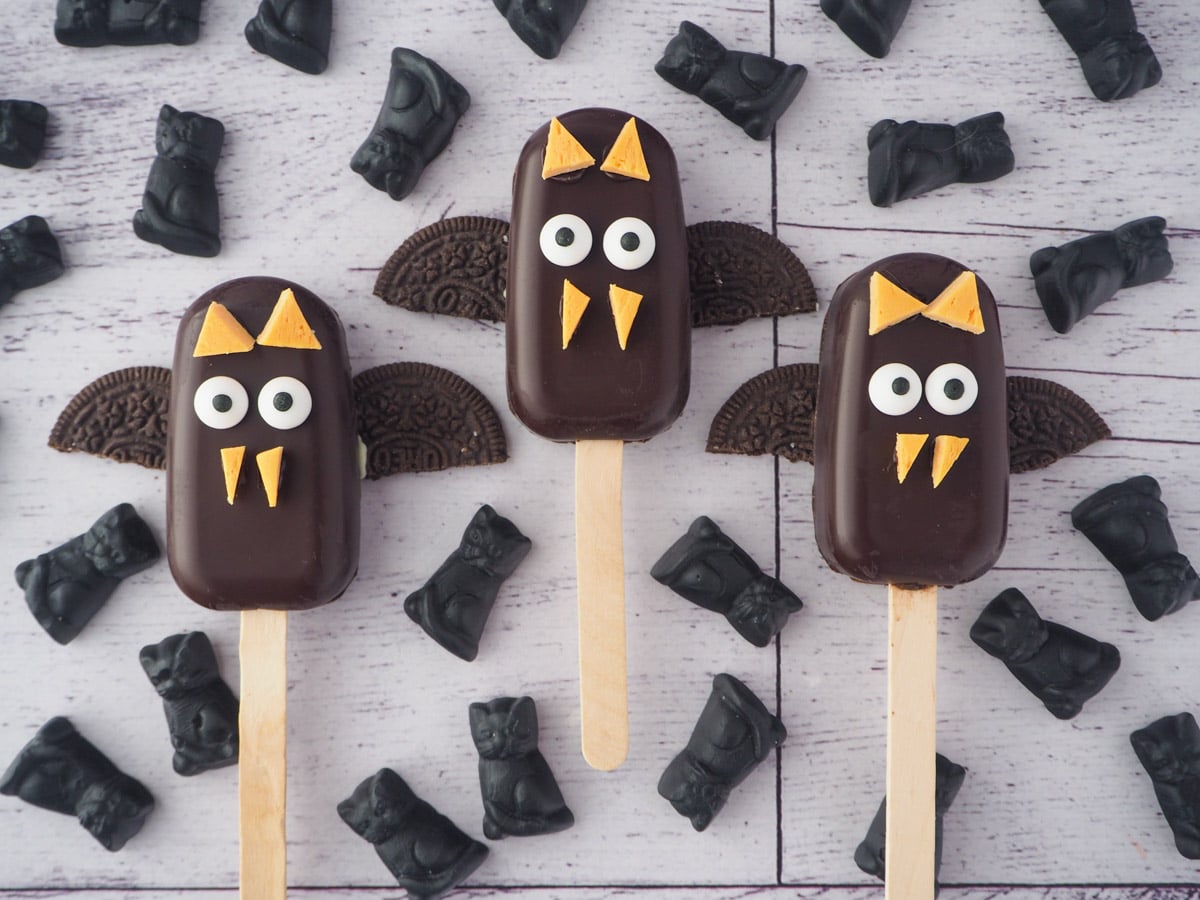 Row of three bat cakesicles surrounded by candy cats.
