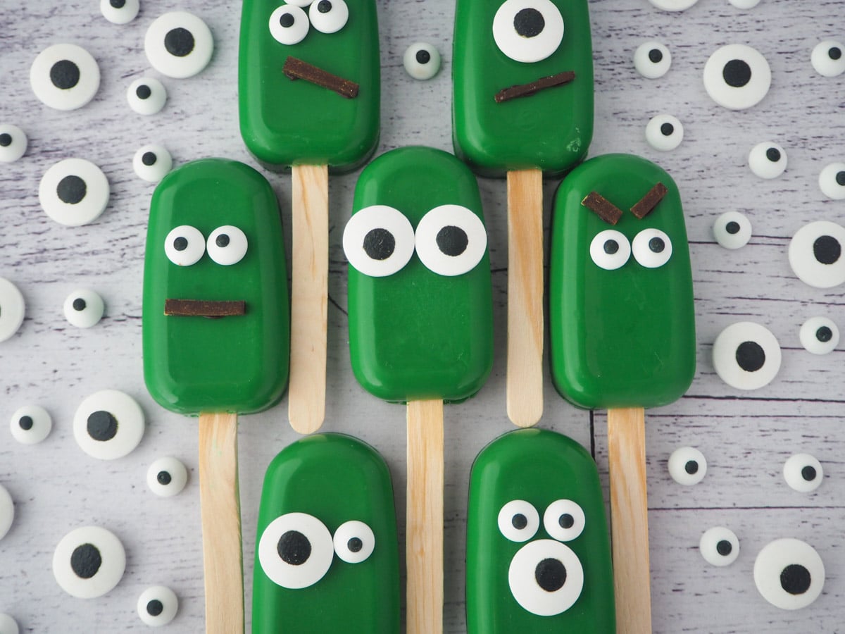 Row of six monster cakesicles, all different, surrounded by candy eyes.