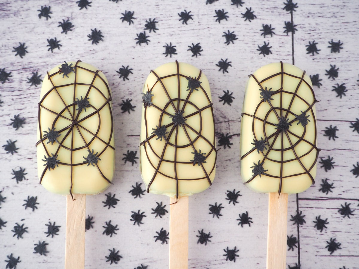 Row of three spider cakesicles, surrounded by spider sprinkles.