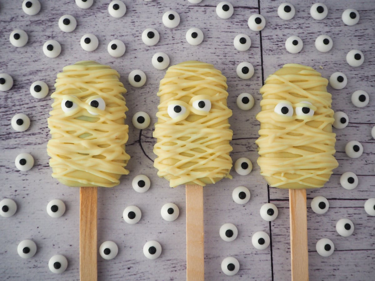 Halloween cakesicles 5 Row of three mummy cakesicles, surrounded by candy eyes.