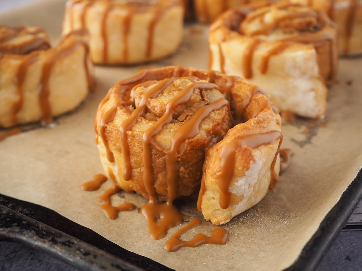 Biscoff Cinnamon Rolls 14 Biscoff roll drizzled with Biscoff on a baking tray.