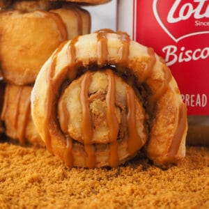 Close up Biscoff scroll on a board with cookie crumbs, with a stack of scrolls and BIscoff jar behind it.