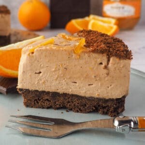 Close up Slice of cheesecake with fork, fresh oranges and dark chocolate in the background.