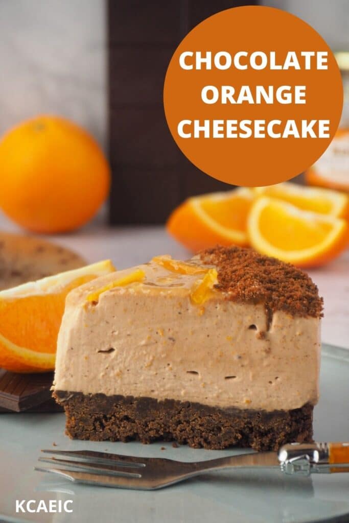 Slice of cheesecake with fork, fresh oranges and dark chocolate in the background and text overlay, chocolate orange cheesecake and KCAEIC.