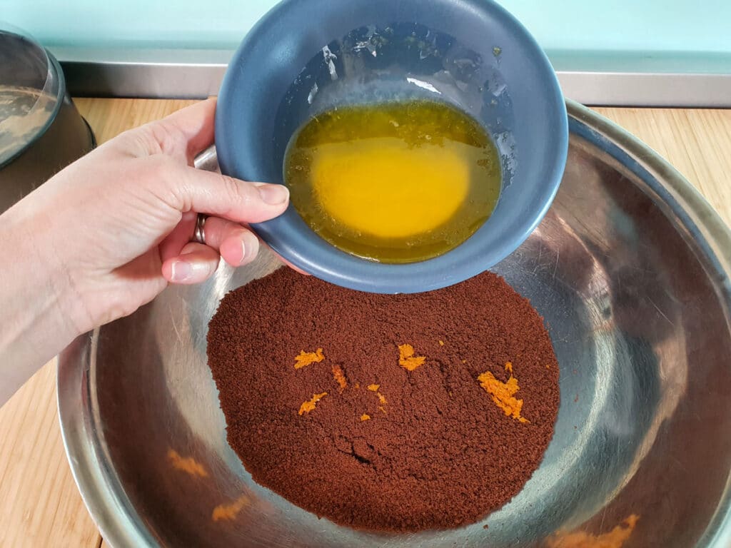Adding the melted butter to the cookie crumbs and orange zest.
