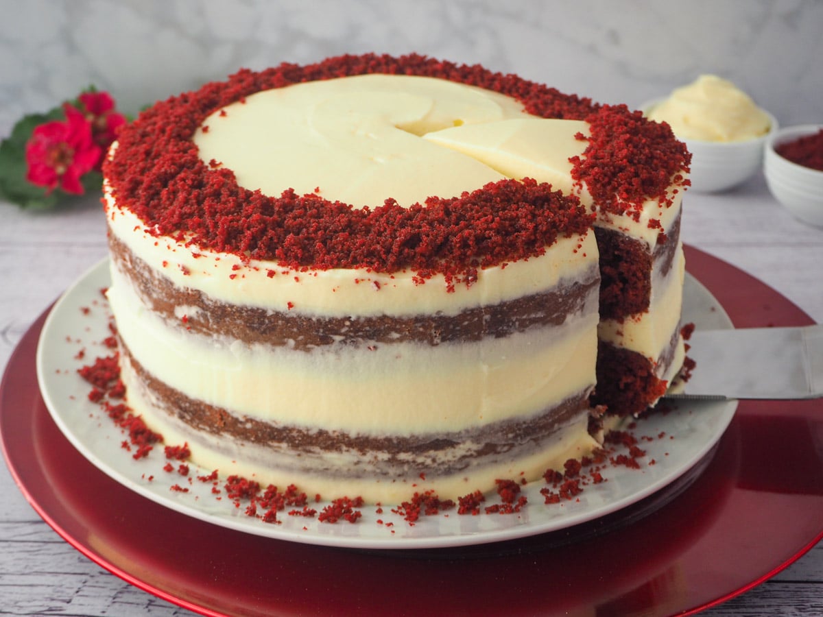 Chocolate Red Velvet Cake 4 Slicing and serving cake, with flowers, frosting and cake crumbs in the background.