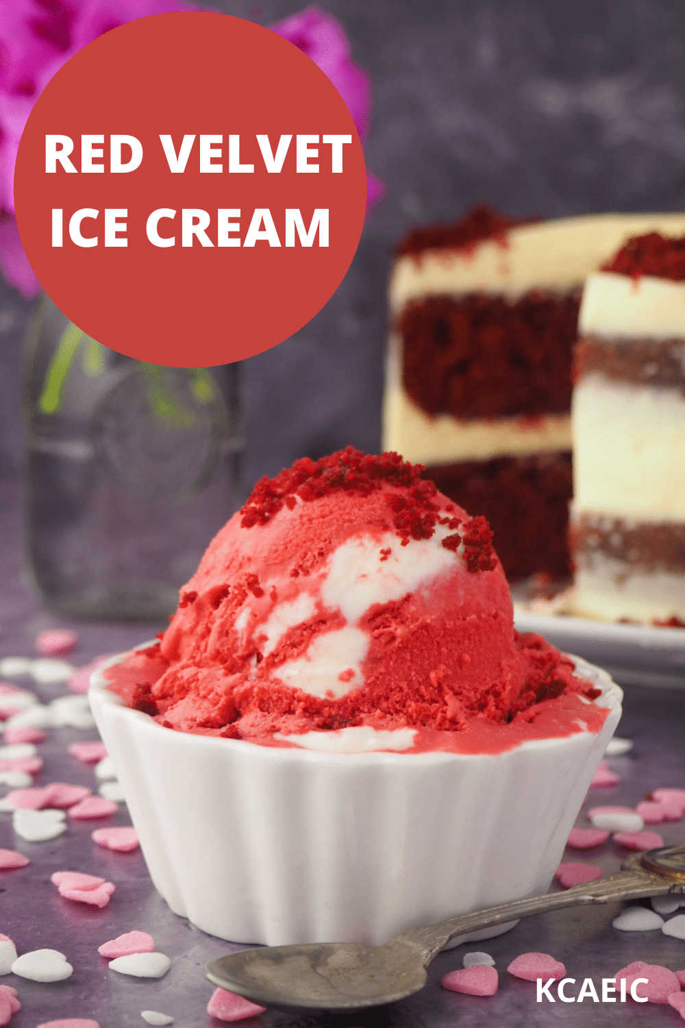 Red velvet ice cream with spoon, and red velvet cake and pink flowers in the background, with text overlay, red velvet ice cream and KCAEIC.