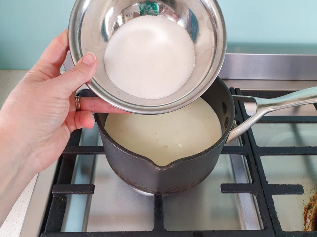 Adding sugar to pot on stove.