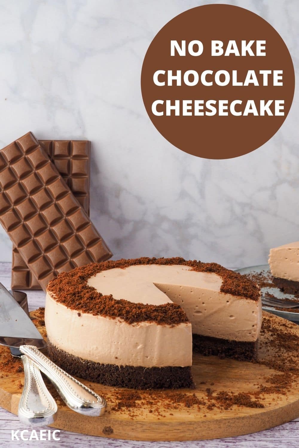 Cheesecake on a serving board with serving wear and slice of cheesecake and block of chocolate in the background, with text overlay, no cake chocolate cheesecake and KCAEIC.