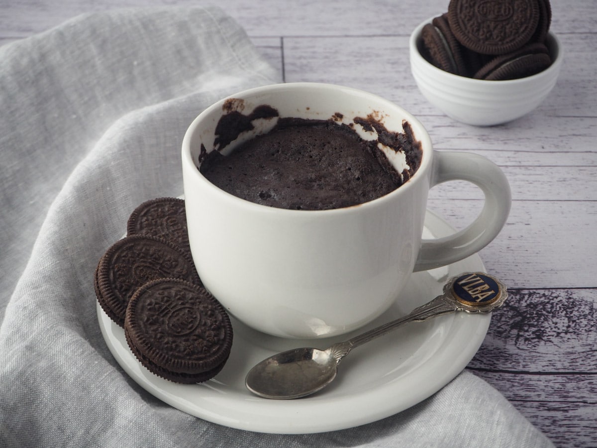 Oreo mug cake on a saucer with a spoon and Oreos on the side and in the background.