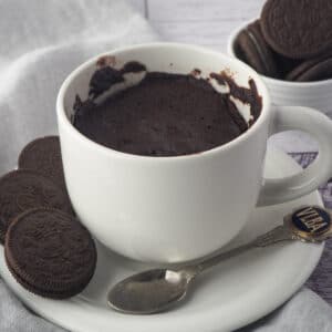 Oreo Mug Cake 16 Close up mug cake on a saucer with a spoon and Oreos on the side and in the background.