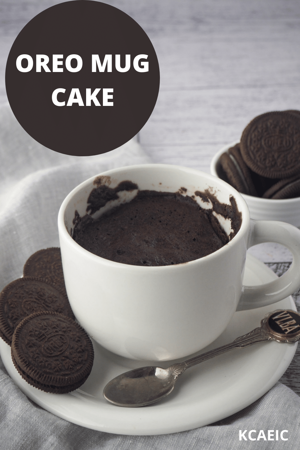 Oreo Mug Cake 17 Mug cake on a saucer with a spoon, Oreos on the side and in the background, with text overlay, Oreo Mug Cake and KCAEIC.