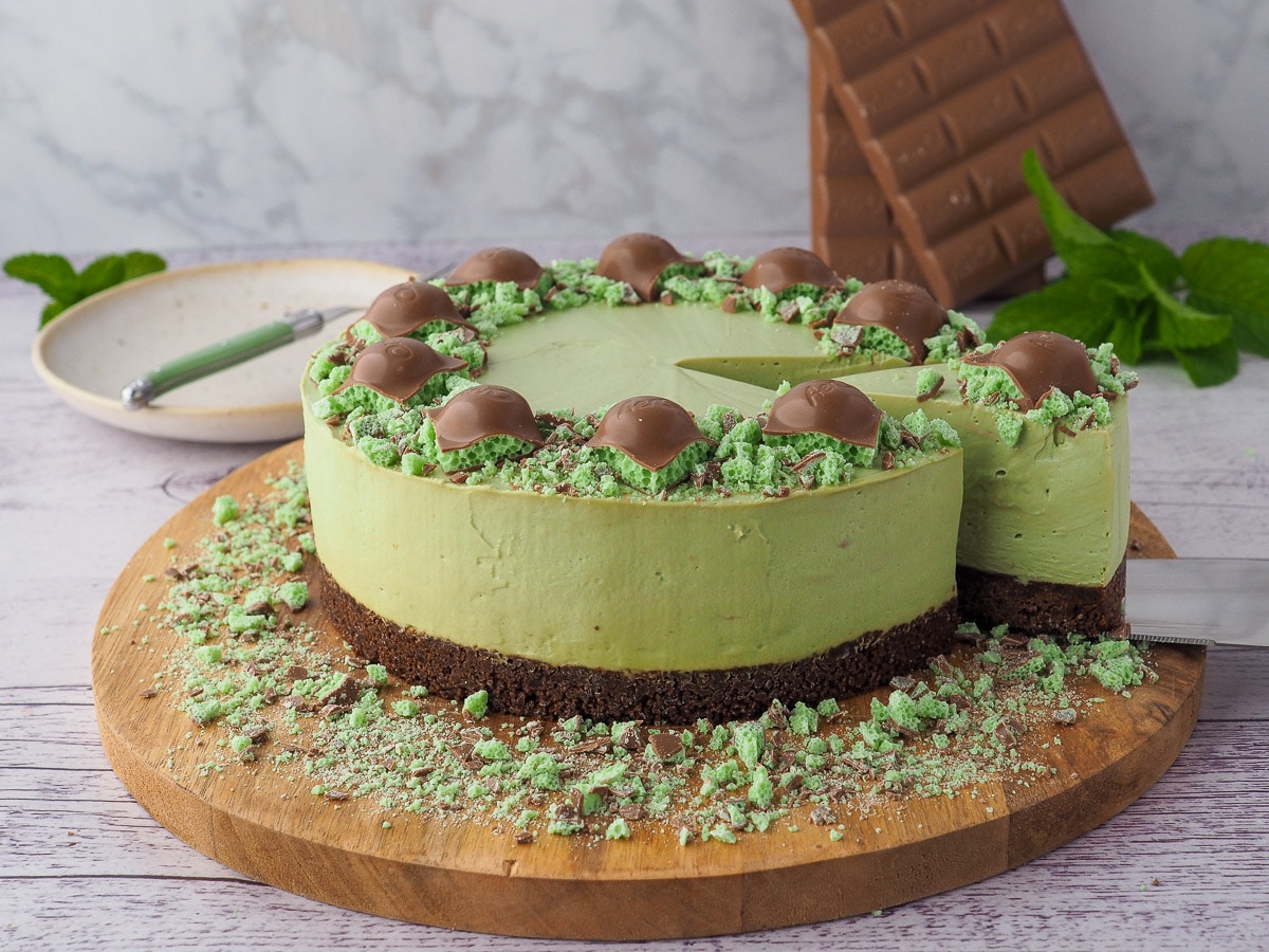 Slicing cheesecake, with plate and fork and chocolate in the background.