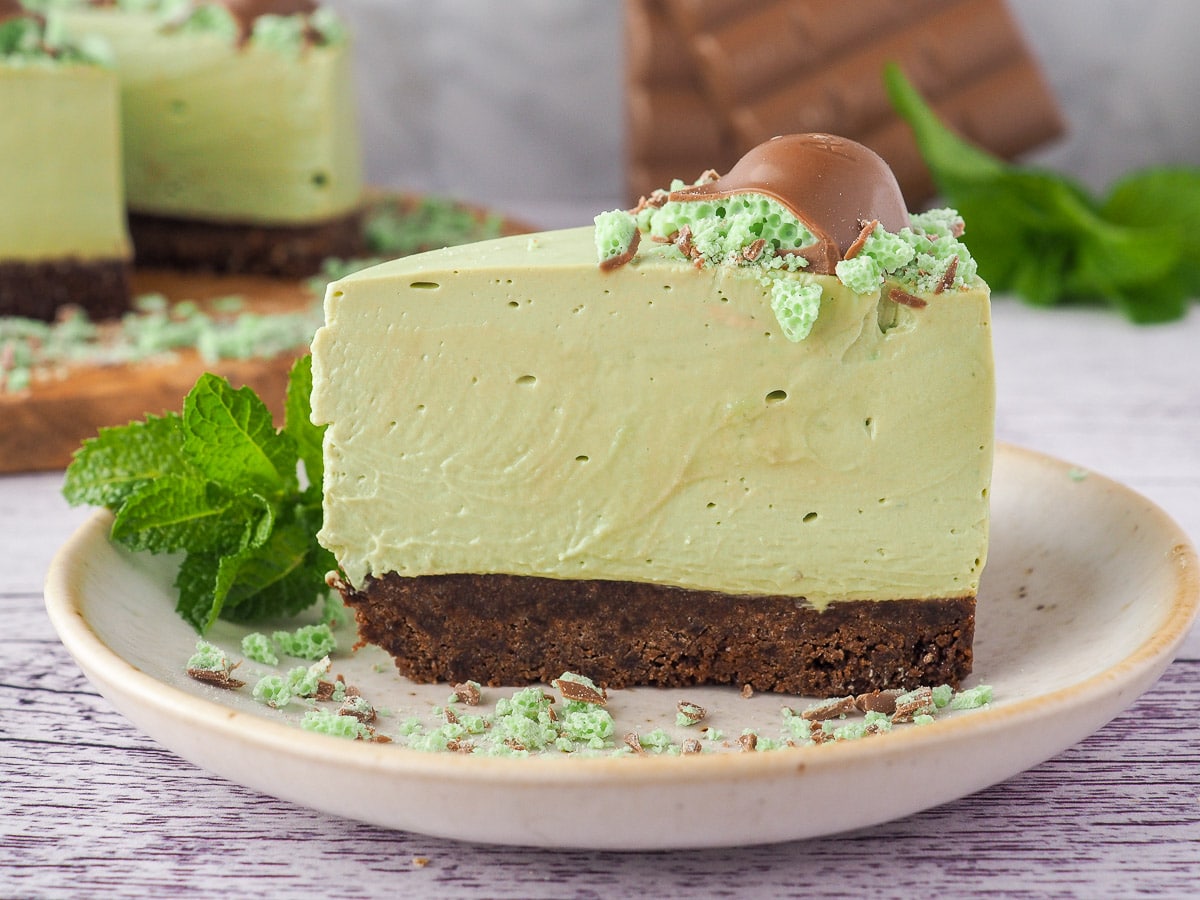 Aero Mint Cheesecake 2 Slice of cheesecake on a plate, with cake and chocolate in the background.
