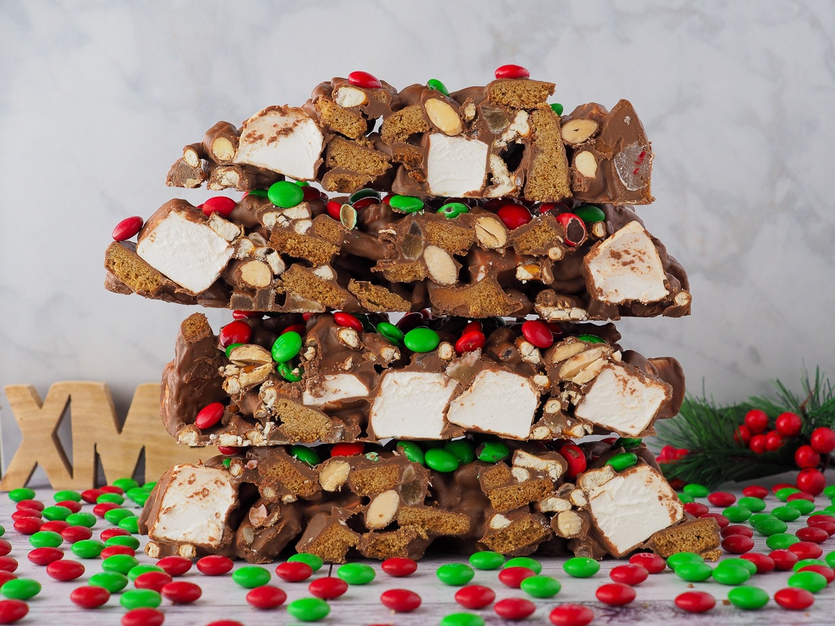 Stack of rocky road with red and green candy and Christmas decorations in the background.