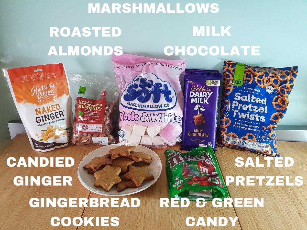 Ingredients, candied ginger, roasted almonds, gingerbread cookies, marshmallows, milk chocolate, salted pretzels, red and green candy.