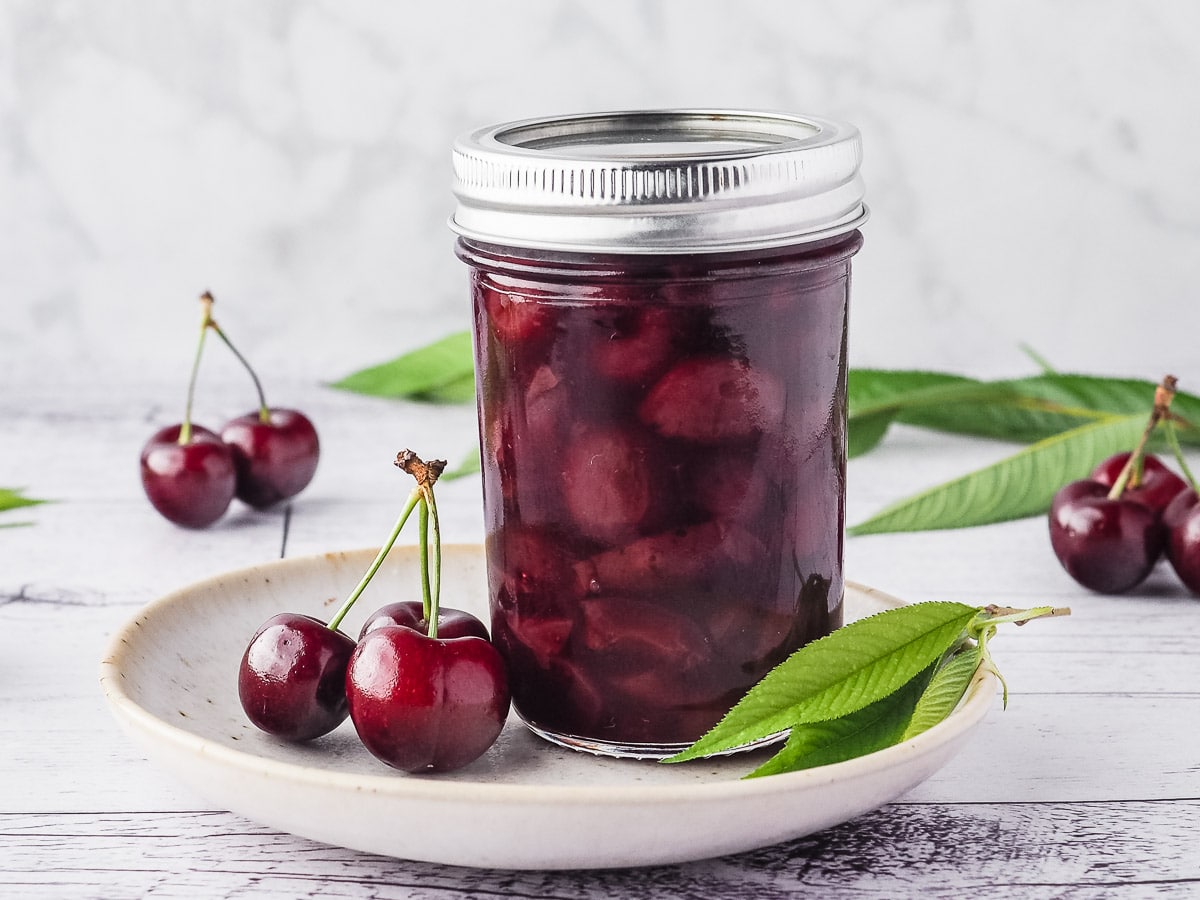 Compote in a mason jar on a plate, with fresh cherries and leaves.