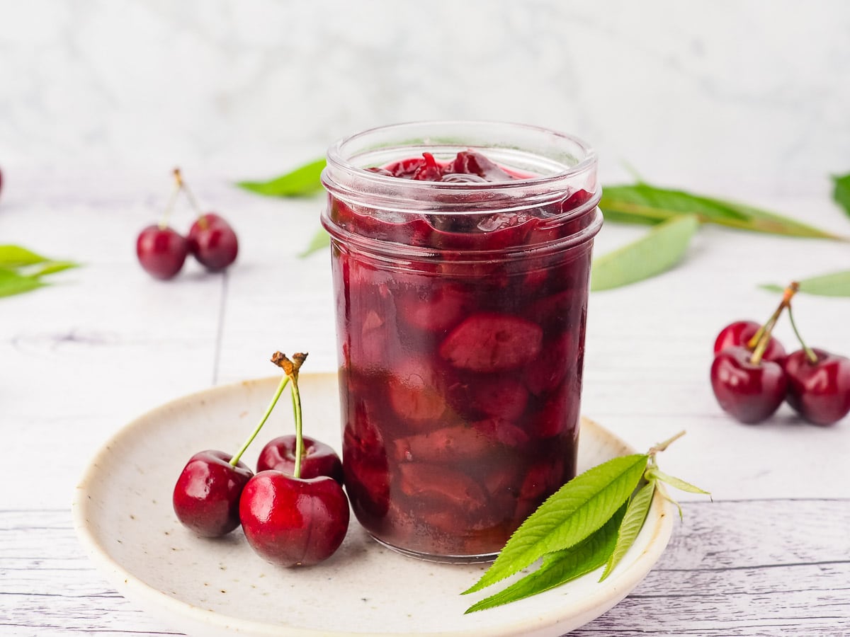 Compote in a mason jar on a plate, with fresh cherries and leaves.