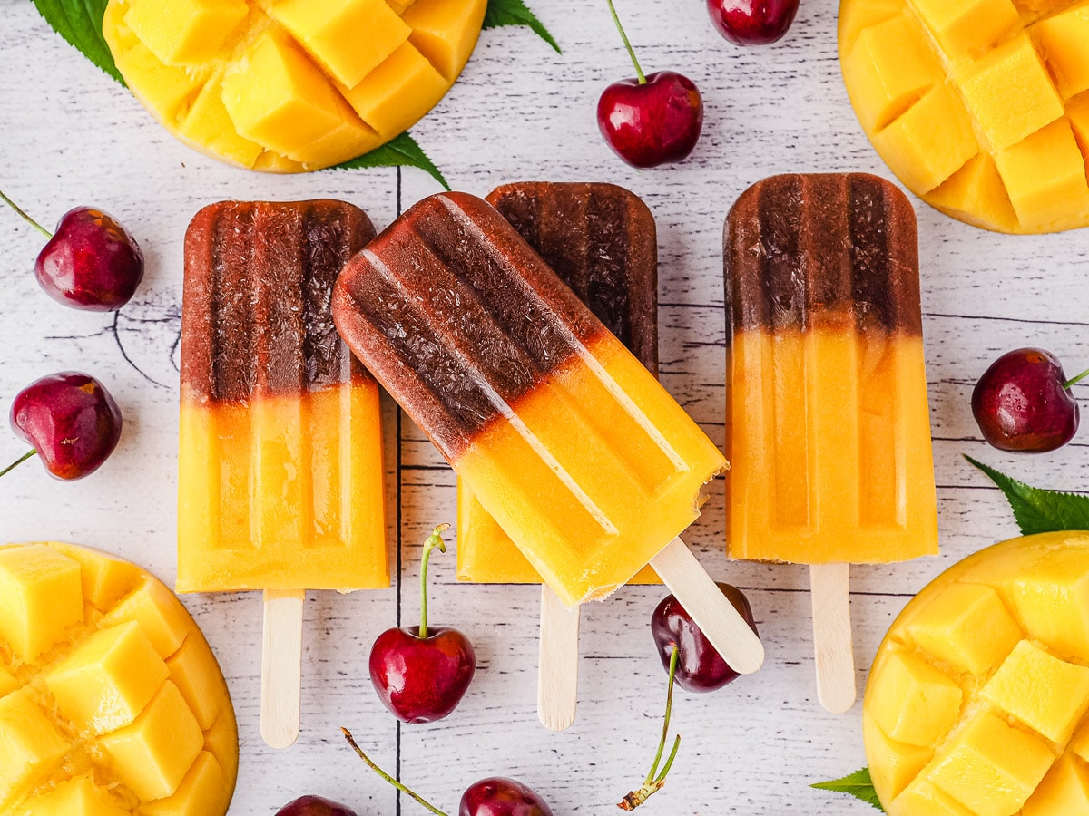 Cherry Mango Popsicles 6 Stack of popsicles surrounded by fresh cherries and mango.
