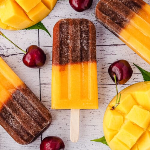 Close up Popsicles surrounded by fresh cherries and mango.