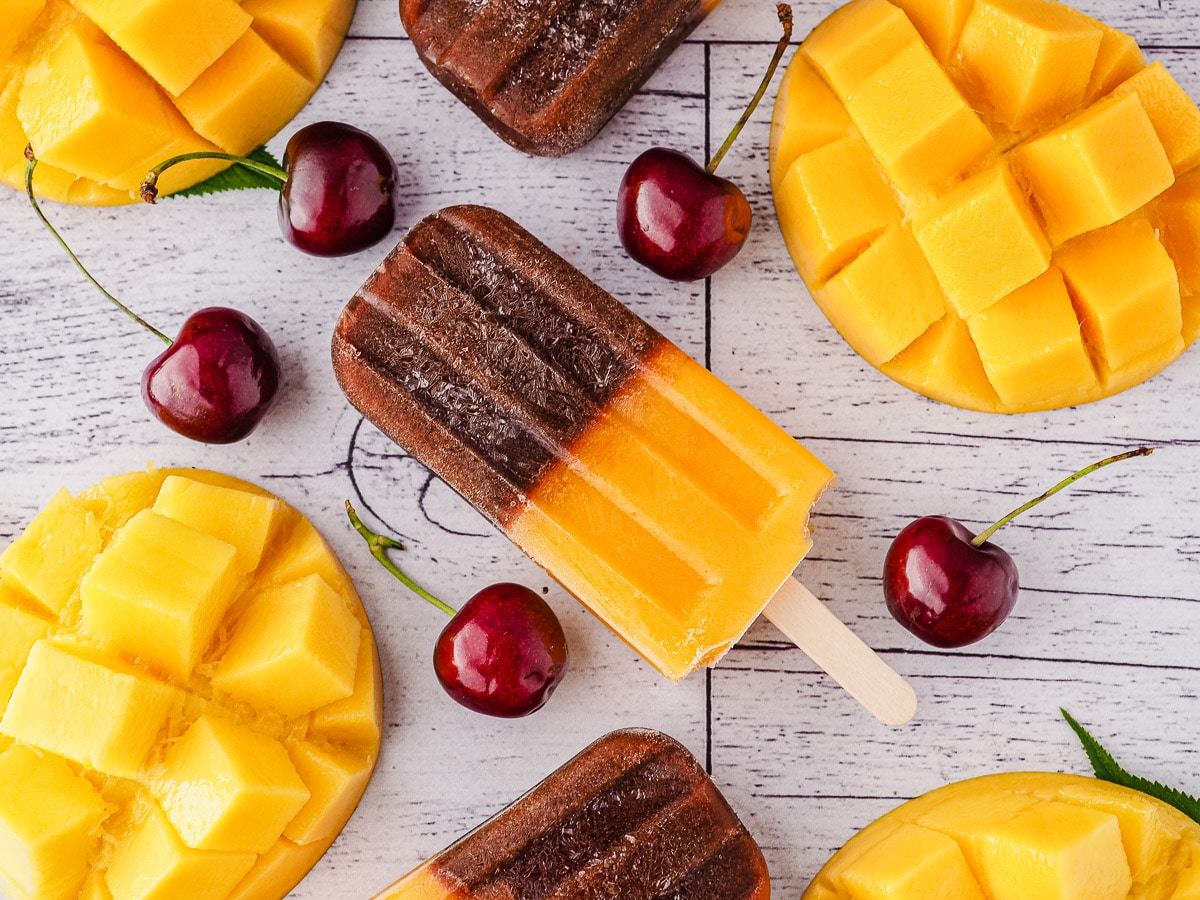 Popsicles surrounded by fresh cherries and mango