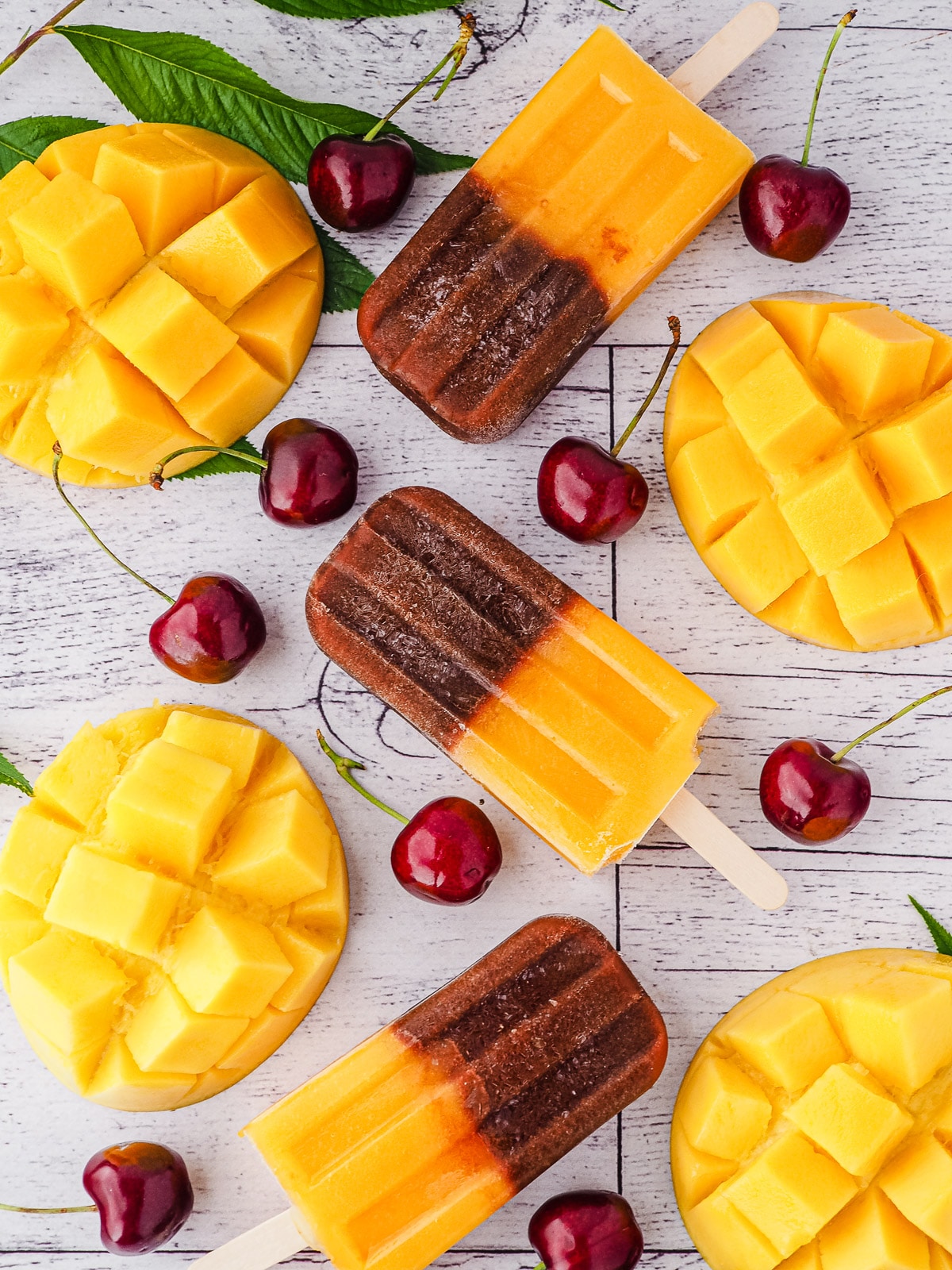 Popsicles surrounded by fresh cherries and mango.