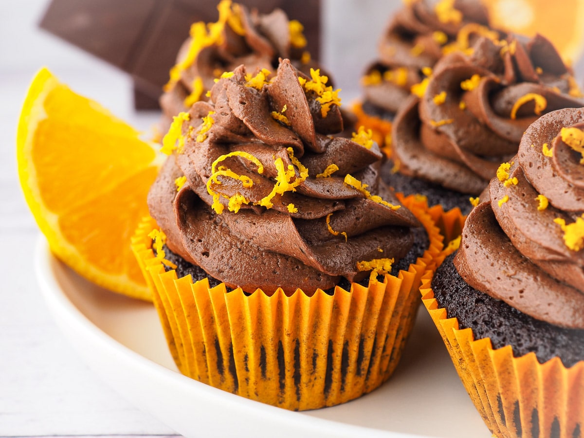 Chocolate Orange Cupcakes 9 Cupcakes on a plate with chocolate and fresh oranges in the background.