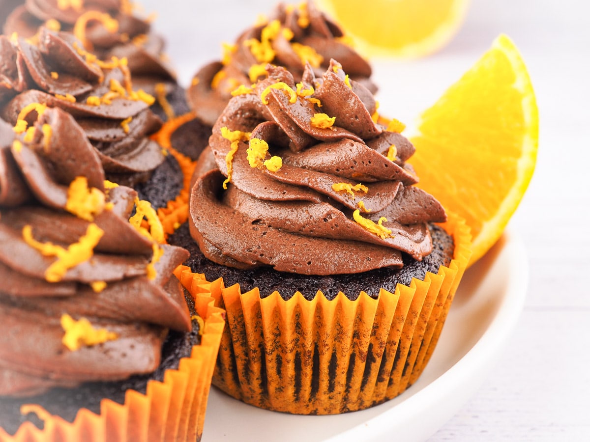 Cupcakes on a plate with chocolate and fresh oranges in the background.