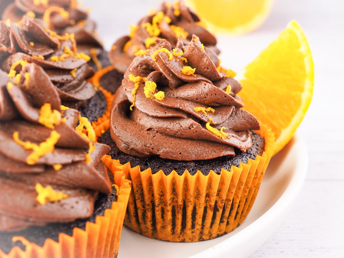 Chocolate Orange Cupcakes 8 Cupcakes on a plate with chocolate and fresh oranges in the background.